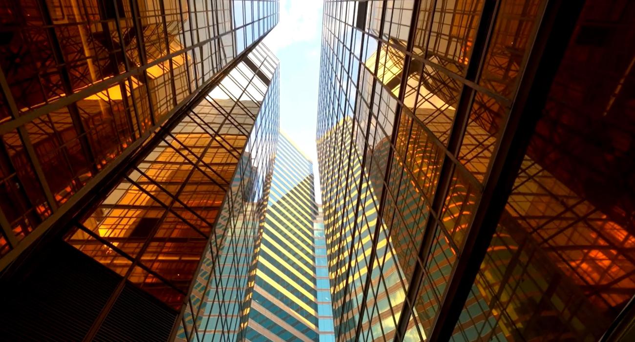 Looking up between two reflective glass buildings with golden hues, showing a clear sky above.